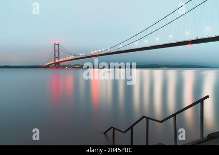 The Humber bridge lit up by bright colorful lights reflecting on the estuary just dawn breaks in Hessle, Yorkshire, UK. Stock Photo