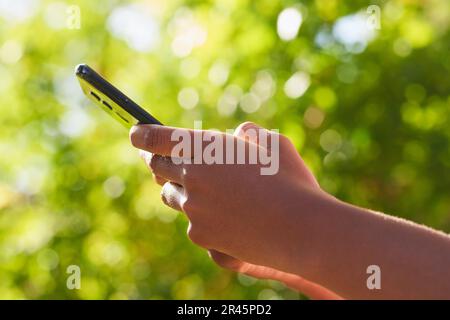 Close up of Black woman's hands using mobile phone, texting in nature leaf bokeh Stock Photo