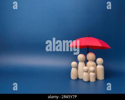 Six small wooden toy figurines against the miniature red umbrella against a blue wall - copy space Stock Photo