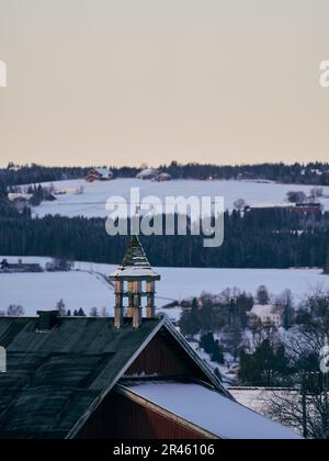 A stunning aerial shot of an old rustic building with a snow-covered roof on a wide open snowy field Stock Photo