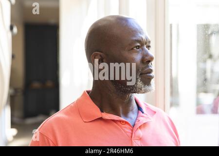 Thoughtful, happy senior african american man standing looking out of window at home Stock Photo