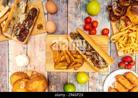 set of latin fast food dishes with a beef sandwich with pieces of fried plantain, fruits, vegetables and empanadas Stock Photo
