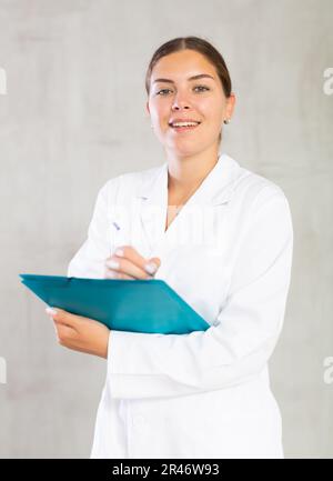 Happy female doctor standing and making notes in file Stock Photo