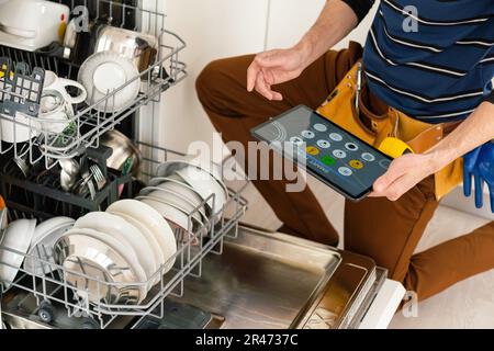 Portrait Of Male Technician Repairing Dishwasher In Kitchen using digital tablet. Stock Photo