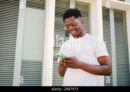 Portrait of smiling young african american man using his smartphone for messaging in social media, watching funny news. Handsome millennial male connecting or browsing on internet with a mobile phone. High quality photo Stock Photo