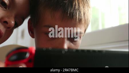 Children absorbed by video-game screen gadget. Young boy playing game online, sibling watching brother play Stock Photo