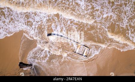 Bird's eye view of a sunken small fishing boat buried in the sand on the coast of the Caribbean Sea, discovered by the waves Stock Photo