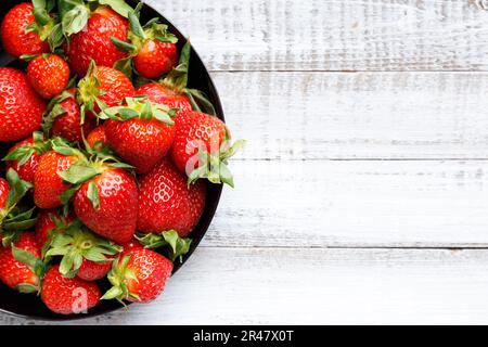 Fresh organic strawberries in a black round plate on a light wooden background, top view, with space for text. Stock Photo