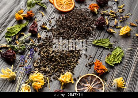 Composition of dry black and green tea, dried citrus slices, mint leaves and dry hibiscus, calendula, lavender flowers on a dark wooden background Stock Photo