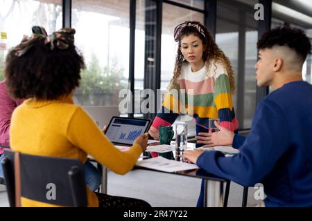 Busy diverse fashion designers using laptop and discussing work at meeting in office, unaltered Stock Photo