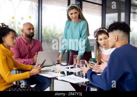 Busy diverse fashion designers using laptop and discussing work at meeting in office, unaltered Stock Photo