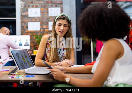 Diverse fashion designers discussing and using laptop at meeting in creative office, unaltered Stock Photo