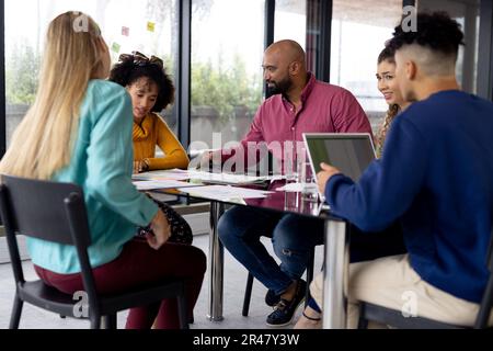 Busy diverse fashion designers using laptop and discussing work at meeting in office, unaltered Stock Photo