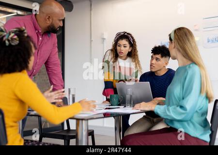 Busy diverse fashion designers using laptop and discussing work at meeting in office, unaltered Stock Photo