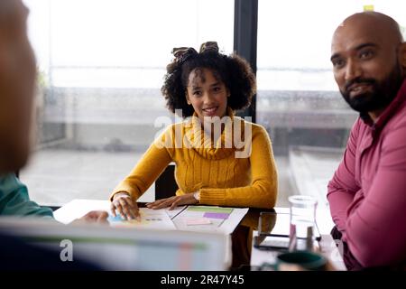 Busy diverse fashion designers using laptop and discussing work at meeting in office, unaltered Stock Photo