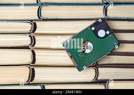 The hard drive of the computer lies on a pile of shabby paper books Stock Photo