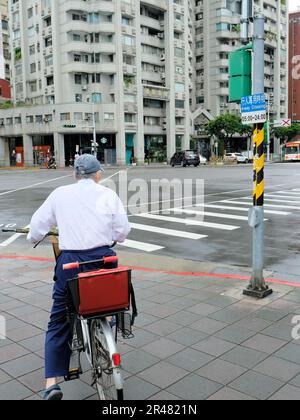 Bicycle rider stopped at a traffic light with a four way crossing sign on metal pole; buses, cars, and motor scooters, Da'an District, Taipei, Taiwan. Stock Photo