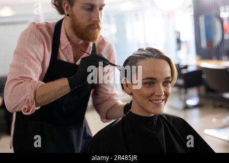 Focused caucasian male hairdresser dyeing hair of happy female client in hair salon Stock Photo