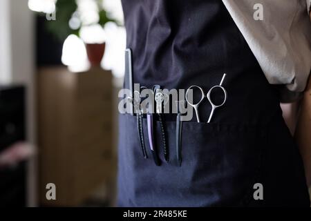 Midsection of caucasian male hairdresser wearing black apron with hairdressing tool in front pocket Stock Photo