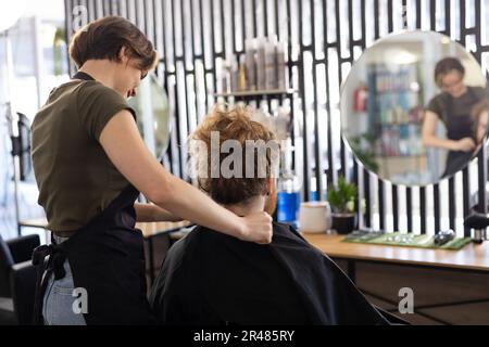 Caucasian female hairdresser putting cape on male customer before working at barbershop Stock Photo