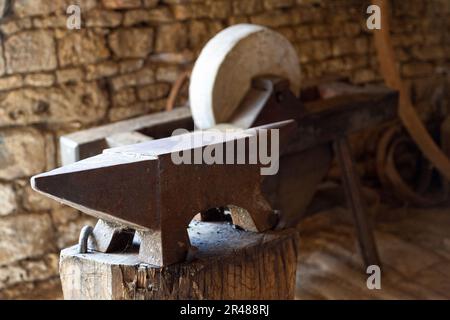 Anvil on its support with behind, a grinding wheel to sharpen the knives and tools. Stock Photo