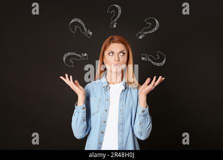 Choice in profession or other areas of life, concept. Making decision, thoughtful woman surrounded by drawn question marks on black background Stock Photo
