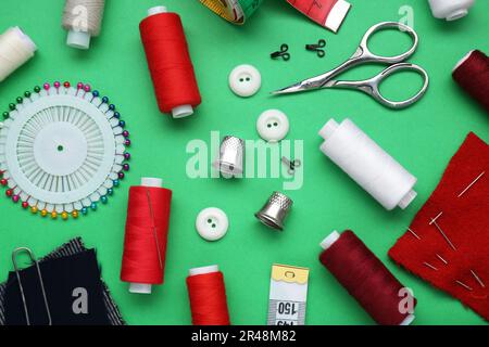 Flat lay composition with thimbles and different sewing tools on green background Stock Photo