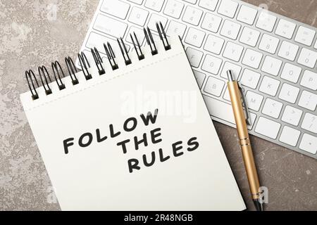 Notebook with phrase Follow The Rules, pen and computer keyboard on grey table, flat lay Stock Photo