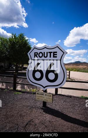 A large, white highway sign stands in the middle of a field of dirt, surrounded by a tall metal fence Stock Photo