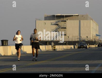 US Navy Mid'n 1st Class and Cadet 2nd Class an exchange student from West Point, jog past the U.S. Navy Barracks Craft Auxiliary Personnel Lighter Sixty One (APL-61) moored along Stock Photo