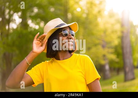 A cheerful black female wearing sunglasses and a hat outdoors in the park on a sunny day Stock Photo