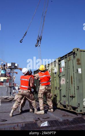 US Navy Members assigned to Naval Expeditionary Logistics Support Force Forward Alpha, move cables into place to attach to cargo containers being off-loaded from the Military Sealift Command (MSC) fast sealif Stock Photo