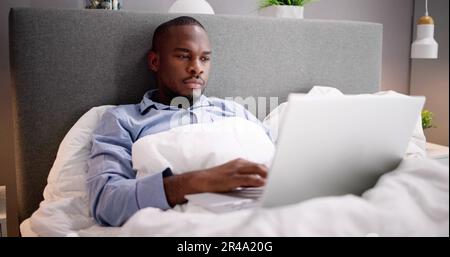 Happy Man Sitting On Bed Using Laptop Stock Photo