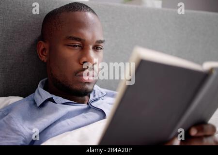 Happy Young African Man Reading His Book On Bed Stock Photo