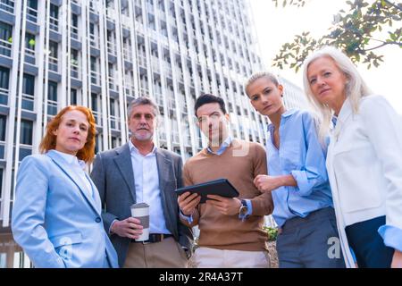 Five business professionals gathered around a tablet, discussing a project and looking at the camera Stock Photo