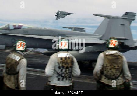 US Navy Flight deck personnel look on as an F-14D Tomcat performs a high-speed fly-by Stock Photo
