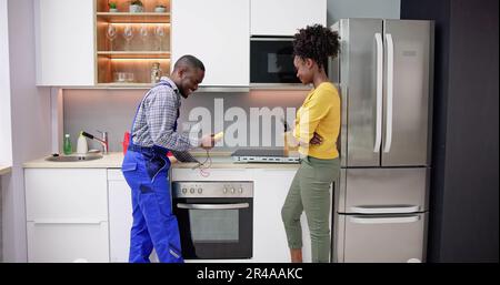 Male Repairman Installing Induction Cooker With Woman Standing In Kitchen Stock Photo