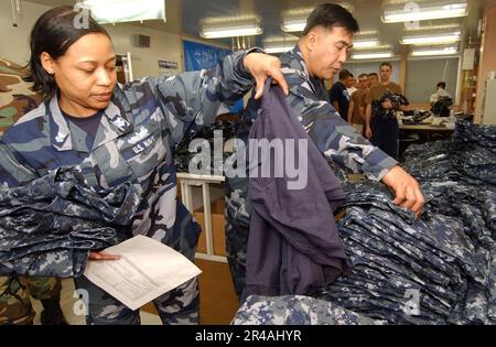 US Navy Yeoman 1st Class left, assigned to the Administration Department on board Naval Air Facility Atsugi, Japan, sorts through a pile of the new Navy Working Uniforms Stock Photo