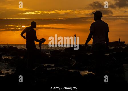 Salvador, Bahia, Brazil - December 11, 2021: Silhouette of fishermen fishing on top of rocks at Rio Vermelho beach in Salvador in late afternoon. Stock Photo