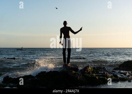 Salvador, Bahia, Brazil - December 11, 2021: A fisherman on top of the rocks fishing. Late afternoon at Rio Vermelho beach in Salvador, Bahia. Stock Photo