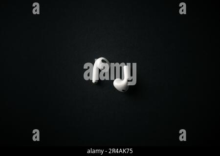 An image of a pair of white earbuds sitting on a black, flat surface in a dark room Stock Photo