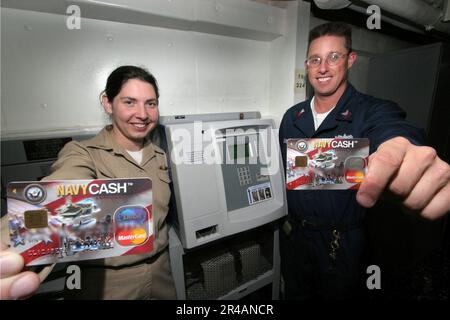 US Navy Disbursing Officer, Lt.j.g. left, and Disbursing Clerk 1st Class display their Navy Cash Cards in front of a K80 terminal aboard the guided missile cruiser USS Lake Stock Photo