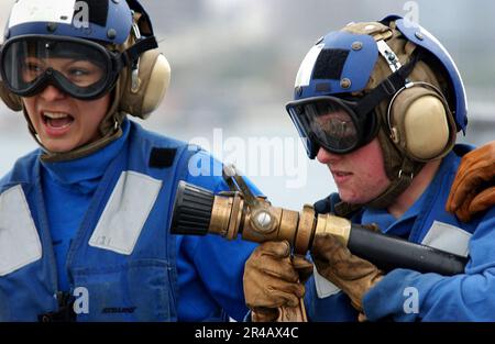 US Navy  Hose Team Leader, Airman left, shouts a verbal command to nozzleman, Airman to combat a simulated aircraft fire during a flight deck drill aboard the Nimitz-class aircraft car. Stock Photo