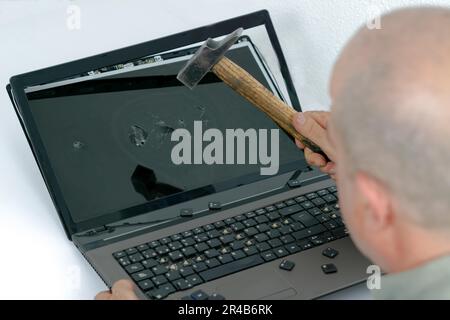 Angry man seen in profile breaking a laptop with a hammer, white background and copy space Stock Photo