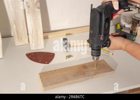 Woman's hands drilling a wooden board with an electric drill on a white board in her workshop Stock Photo