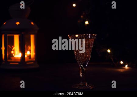 Glass with white wine with garland lights and candle lantern on the background. dark picture. Burning candle. Golden beverage in the glass. Beautiful Stock Photo