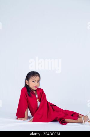 A young woman in a stylish red dress is sitting with one leg extended in the air, her arms crossed and her head tilted as if in thought Stock Photo