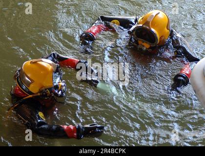 US Navy  U.S. Navy divers, assigned to Mobile Diving and Salvage Unit Two (MDSU-2), Detachment Two, swim alongside a U.S. Coast Guard patrol boat after repairing the vessel's damaged rudder and propeller. Stock Photo