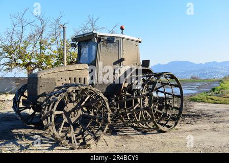 An aged tractor sits abandoned on the roadside, its rusting exterior and weathered features creating an interesting contrast to the foliage in the bac Stock Photo
