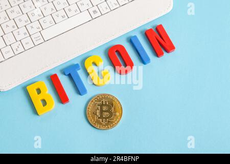 Cryptocurrency for kids. White keyboard, Bitcoin word from colorful letters on blue background Stock Photo